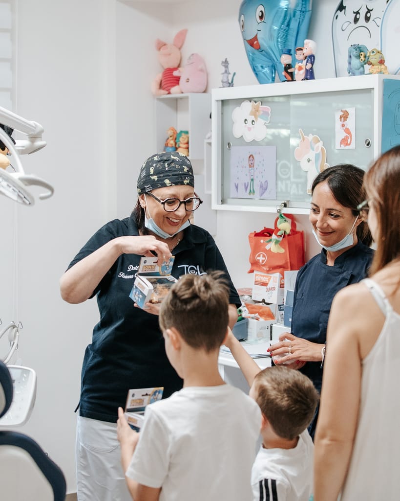 La Dott.ssa Tiziana Catalfamo consegna un regalo a due bambini accompagnati dalla mamma, nella sala di TCL Dental